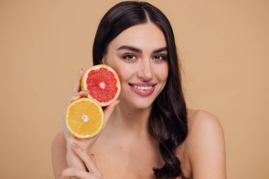 Genç bir kadının portresi, portakal rengi greyfurt gülümseyen dişlerin yarısını beslenen vejetaryen vitamin yaz vitamini, saç bakımı, doğal organik vegan narenciye bej arka planda.