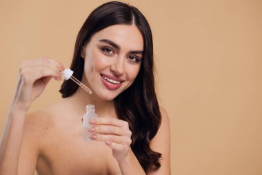 Bej arka planda Serum Bırakan Kadın. Pipette 'ten Serum Kolajeni Nemlendirici kullanan Avrupalı Kız. Yakın plan. Pozitif Gülen Güzel Kadın Portresi. Yüz Cildi Bakımı Konsepti