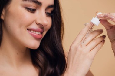 Bej arka planda Serum Bırakan Kadın. Pipette 'ten Serum Kolajeni Nemlendirici kullanan Avrupalı Kız. Yakın plan. Pozitif Gülen Güzel Kadın Portresi. Yüz Cildi Bakımı Konsepti