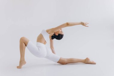 Zayıf vücutlu sporcu bir kadının beyaz arka planda izole edilmiş yoga pratiği yaparken tam boy görüntüsü. Vücut ve zihinsel gelişim arasındaki sağlıklı yaşam ve doğal denge kavramı.