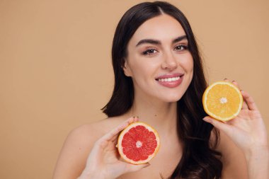 Genç bir kadının portresi, portakal rengi greyfurt gülümseyen dişlerin yarısını beslenen vejetaryen vitamin yaz vitamini, saç bakımı, doğal organik vegan narenciye bej arka planda.