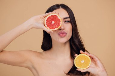 Genç bir kadının portresi, portakal rengi greyfurt gülümseyen dişlerin yarısını beslenen vejetaryen vitamin yaz vitamini, saç bakımı, doğal organik vegan narenciye bej arka planda.