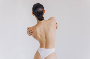 Arkası kesilmiş, ince vücutlu, mükemmel ciltli, çıplak, sütyen giysili genç bir bayan beyaz arka planda izole edilmiş kalçalara el ele tutuşuyor. Yaşam tarzı diyet konsepti