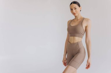 Beyaz arka planda bej renkli spor giysili zayıf bir kadın izole edilmiş. Düz göbekli, kaslı, zayıf, çekici bir kadın. Uzayı metin için kopyala. Vücut bakımı, sağlıklı ve sportif yaşam, saç aldırma, yoga konsepti