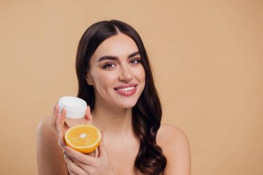 Kadın, doğal cilt bakımı için nemlendirici krem ve turuncu ve bej renkli stüdyo arka planına karşı C vitamini. Sağlıklı organik ürünler için meyve ve krem ya da losyon tutan mutlu kadın portresi