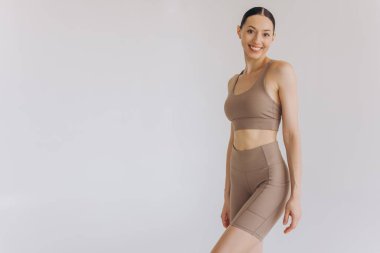 Beyaz arka planda bej renkli spor giysili zayıf bir kadın izole edilmiş. Düz göbekli, kaslı, zayıf, çekici bir kadın. Uzayı metin için kopyala. Vücut bakımı, sağlıklı ve sportif yaşam, saç aldırma, yoga konsepti