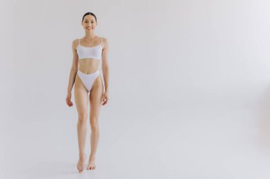 İnce vücutlu, beyaz stüdyo arka planında fotokopi aletiyle poz veren güzel bir kadının tam boy portresi.