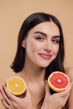 Genç bir kadının portresi, portakal rengi greyfurt gülümseyen dişlerin yarısını beslenen vejetaryen vitamin yaz vitamini, saç bakımı, doğal organik vegan narenciye bej arka planda.