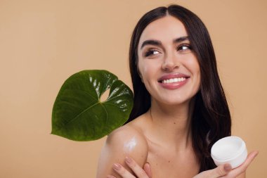 Gülen, yarı çıplak, gülümseyen ve bej arka planda izole edilmiş yüz kremi süren güzel bir kadının güzel portresini kapat.