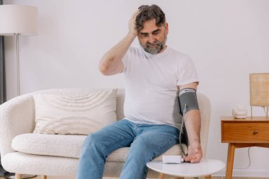 Evdeki kanepede oturmuş, tansiyonunu ölçen, gri saçlı, son sınıf öğrencisi. Modern tonometre kullanan emekli, hipertansiyon deneyimi yaşayan, kopyalama alanı