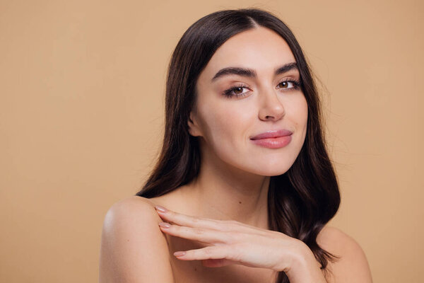 Beautiful young brunette woman with clean fresh skin on beige background, Face care, Facial treatment, Cosmetology, beauty and spa, female smiling portrait