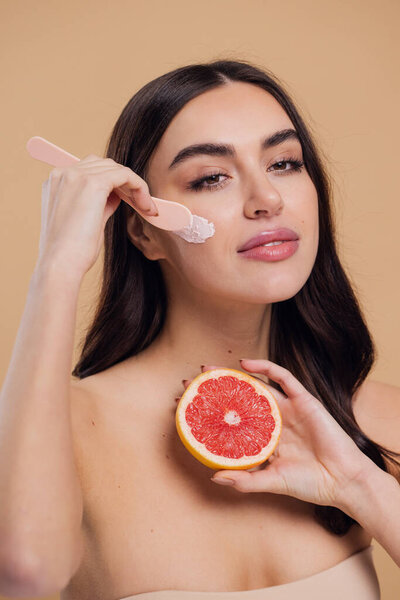 Half naked woman, face and brush cream for beauty, salon and skin care on mock up beige background. Happy model smiling and holding grapefruit, facial lotion and make up cosmetics for dermatology