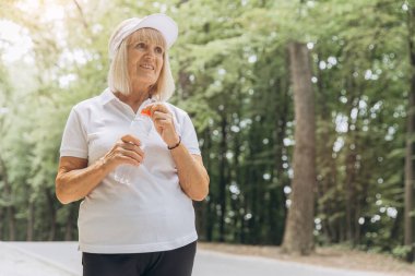 Açık havada egzersiz yaptıktan sonra elinde bir şişe suyla poz veren mutlu ve güzel bir kadının portresi.