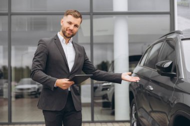 Portre, araba galerisinde gülümseyen adam. Ticari bir otoparkta araba satışı için. İş, lüks ve otomobil ticareti. Nakliye hizmetleri için takım elbiseli, mutlu sakallı bir satıcıyla.