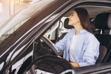 Yeni arabasında oturan mutlu genç kadının fotoğrafı. Araba kiralama konsepti. Bir kadın araba alıyor ve çok mutlu görünüyor. Dışarıya bakan genç bir kadın..