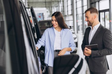 Araba Satış Müdürü, Kafkasyalı Kadın Alıcıya Oto Minivan gösteriyor Lüks Otomobil Galerisinde duruyor. Araç Konsepti Alınıyor