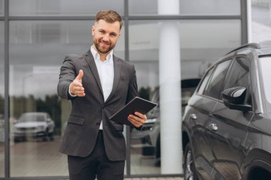 Portre, gülümseyen adam el sıkışmak için ticari bir otoparkta araba satışı için araba galerisinde el sıkışıyor. Ulaştırma hizmeti için pazarlamacıyla iş, lüks ve otomobil ticareti