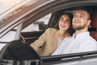 Modern lüks bir arabada oturan gülümseyen güzel bir çiftin portresi mutlu genç adam ve kadın galeriden yeni bir araba alıyorlar..