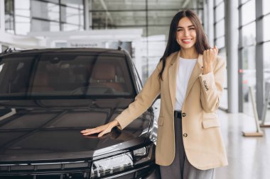Çekici genç beyaz kadın yeni arabanın kaputuna sarılıyor yumruğunu gösteriyor ve modern parlak araba bayiliğinde evet diyor. Mutlu alıcı kız rüyasını gerçekleştirdikten sonra sevinir..