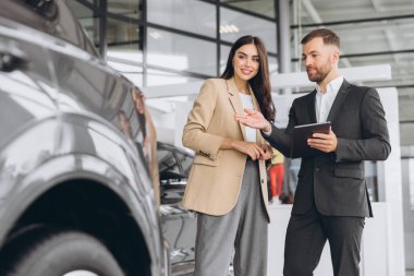 Genç bayan müşteri bayan müşteri bej ceket giyiyor satış elemanı holding tabletine danışarak araba galerisi araç galerisi galerisi galerisi galerisi araba galerisi araba galerisinde yeni otomobil almak istiyor..