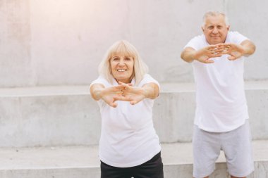 Açık hava ortamında spor yapmayı seven mutlu bir çift. Spor kıyafetleri giyiyorlar ve esneme egzersizleri yapıyorlar. Emekliliklerinde aktif bir yaşam tarzının önemini gösteriyorlar..