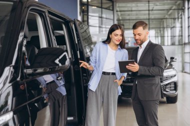 Araba Satış Müdürü, Kafkasyalı Kadın Alıcıya Oto Minivan gösteriyor Lüks Otomobil Galerisinde duruyor. Araç Konsepti Alınıyor