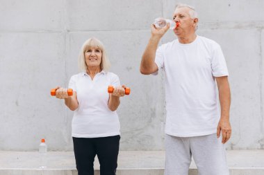 Üst düzey çiftler, halter ve su ile dışarıda egzersiz yaparken sağlıklı bir yaşam tarzını seviyorlar. Fitness, mutluluk ve zindelik sergilerler, aktif yaşlanma ve fiziksel sağlığı destekleyici bir ortamda teşvik ederler..