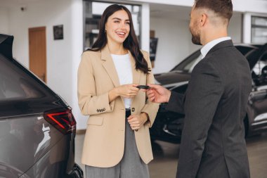 Gülümseyen satıcı ya da müdür modern mutlu kadına araba anahtarı veriyor. Araba galerisinde yeni araba sahibi.