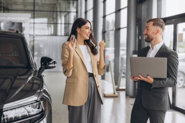 Yeni arabanın anahtarlarını tutan, yumruğunu gösterip modern araba galerisinde evet diyen beyaz bir kadın. Mutlu alıcı kız rüyasını gerçekleştirdikten sonra sevinir..