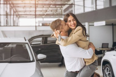 Temsilci olarak yeni otomobilleri olan güzel evli bir çift. Mutlu beyaz adam ve kadın araba aldıktan sonra sarılıyorlar..