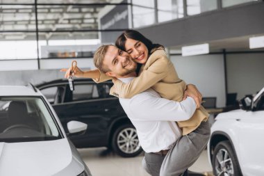 Temsilci olarak yeni otomobilleri olan güzel evli bir çift. Mutlu beyaz adam ve kadın araba aldıktan sonra sarılıyorlar..