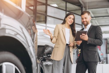 Genç bayan müşteri bayan müşteri bej ceket giyiyor satış elemanı holding tabletine danışarak araba galerisi araç galerisi galerisi galerisi galerisi araba galerisi araba galerisinde yeni otomobil almak istiyor..