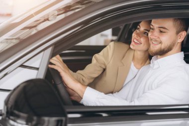 Modern lüks bir arabada oturan gülümseyen güzel bir çiftin portresi mutlu genç adam ve kadın galeriden yeni bir araba alıyorlar..