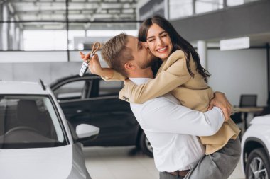 Temsilci olarak yeni otomobilleri olan güzel evli bir çift. Mutlu beyaz adam ve kadın araba aldıktan sonra sarılıyorlar..