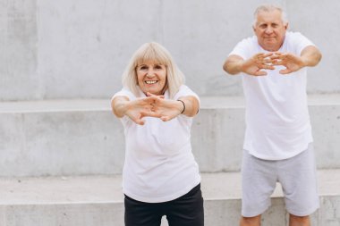 Açık hava ortamında spor yapmayı seven mutlu bir çift. Spor kıyafetleri giyiyorlar ve esneme egzersizleri yapıyorlar. Emekliliklerinde aktif bir yaşam tarzının önemini gösteriyorlar..
