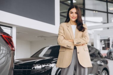 Araba Bayilik ziyaret etti. Güzel genç kadın kameraya bakarak ve çapraz kolları olan dururken yeni arabasını gülümseyen