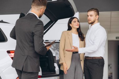 Araba galerisindeki satıcıdan alacakları arabanın bagajını inceleyen güzel bir çift.