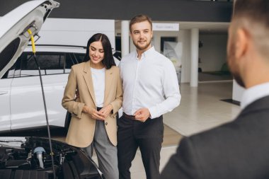 Bir satıcı araba galerisinde beyaz güzel bir çifte kapüşonlu bir araba gösteriyor..