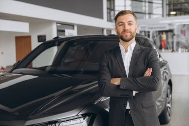 Galeride çalışan yakışıklı bir erkek araba satıcısının portresi. Bir araba galerisinde duran mutlu satıcı.