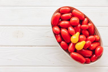 Beyaz ahşap arka planda tek bir sarı domatesli taze kırmızı üzüm domateslerinin üst görüntüsü..