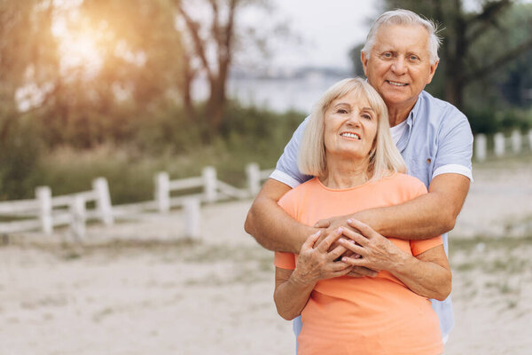 Senior couple embracing outdoors, enjoying a summer day and their retirement time together, expressing love and happiness.