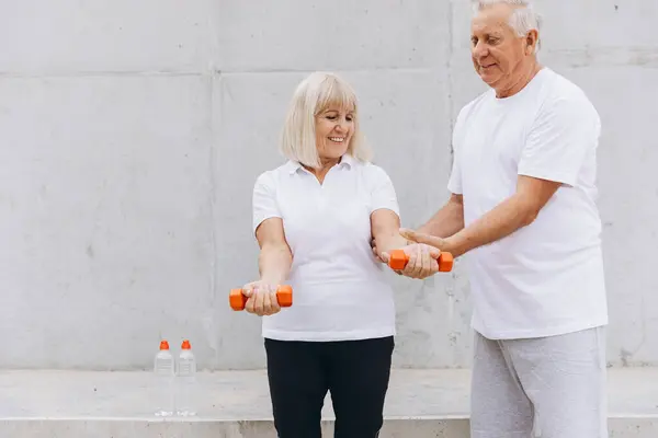 stock image Senior couple exercising together outdoors using dumbbells, promoting a healthy and active lifestyle. They are dressed in casual sportswear, sharing a moment of encouragement and support, illustrating fitness, wellness, and aging gracefully.