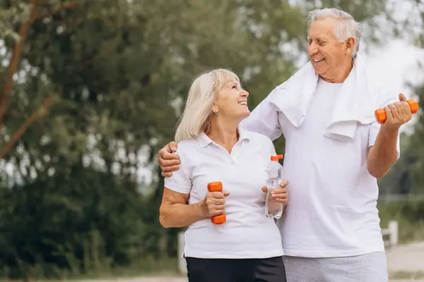 stock image Happy senior couple smiling while exercising outdoors with dumbbells and water bottles, promoting fitness and healthy lifestyle.