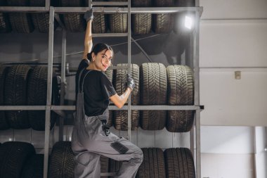 Mutlu kadın araba servisindeki ürün dengesini kontrol etmek için depodaki lastik stoklarını kontrol ediyor.