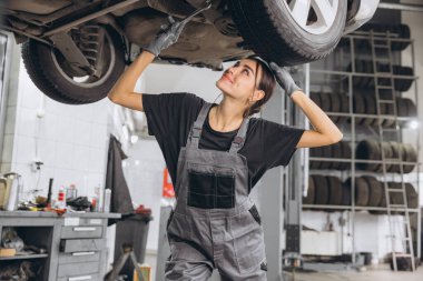 Araba tamirhanesinde araba tamircisi, gri üniformalı kadın tamirci tamirhanede araç bakımı yapıyor..