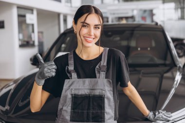 Araba tamirhanesinde kameraya gülümseyen profesyonel kadın tamircinin portresi. Araba servisi, onarım, bakım ve insan konsepti.