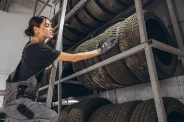 Mutlu kadın araba servisindeki ürün dengesini kontrol etmek için depodaki lastik stoklarını kontrol ediyor.