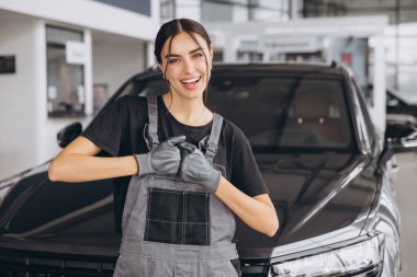 Araba tamirhanesinde kameraya gülümseyen profesyonel kadın tamircinin portresi. Araba servisi, onarım, bakım ve insan konsepti.