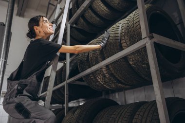 Mutlu kadın araba servisindeki ürün dengesini kontrol etmek için depodaki lastik stoklarını kontrol ediyor.