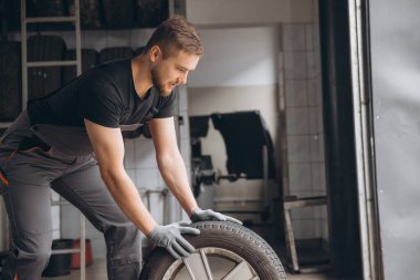 Sakallı tamirci tamirhanede tekerlek lastiği tutuyor. Kış ve yaz lastiklerinin değiştirilmesi
